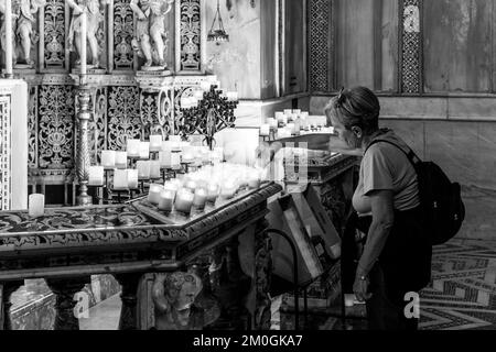 Eine Frau, die eine Kerze in der Kathedrale von Monreale, Palermo, Sizilien, Italien, beleuchtet. Stockfoto