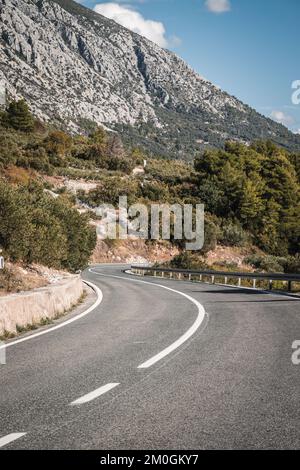 Ein vertikales Bild einer leeren Autobahn, umgeben von dramatischen Bergen an einem sonnigen Tag in Kroatien Stockfoto