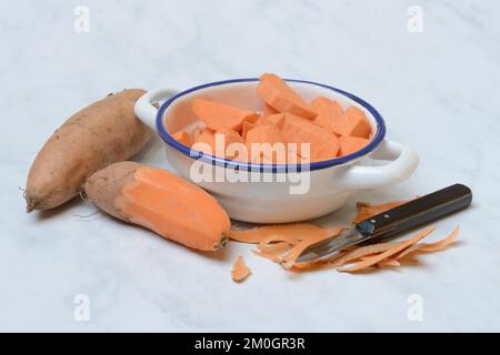 Süßkartoffeln (Ipomoea batatas), Süßkartoffelstücke in der Haut mit Schäler Stockfoto