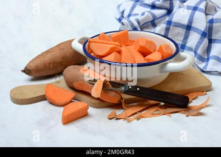 Süßkartoffeln (Ipomoea batatas), Süßkartoffelstücke in der Haut mit Schäler Stockfoto