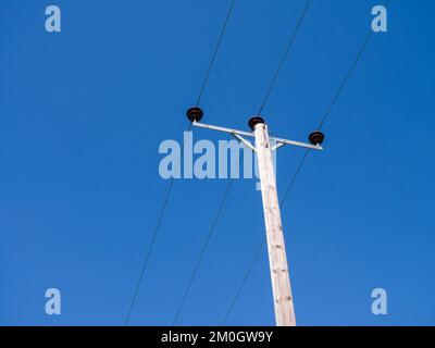 Über dem Holzmast montierte dreiphasige Hochspannungs-Stromverteilerkabel mit 33 kV vor klarem blauem Himmel in Somerset, England. Stockfoto