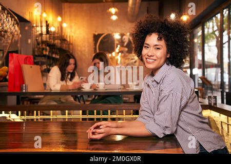 Fröhliche lateinische, mächtige Frau lockiges Haar, die in die Kamera schaut. Freundinnen haben Spaß in einer Bar Stockfoto