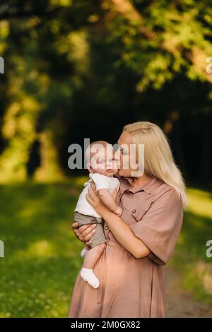 Eine Mutter hält einen glücklichen Jungen in den Armen in einem Sommerpark Stockfoto