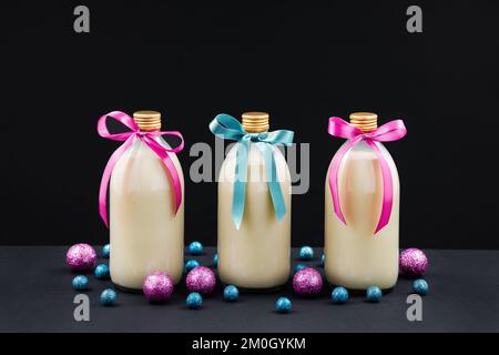 Hausgemachter Eierpunsch in Flaschen mit pinkfarbenen und blauen Kugeln auf dunklem Hintergrund Stockfoto