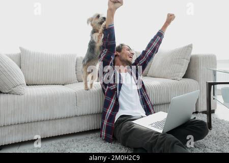 Happy Guy frohlockt mit seinem Hund sitzt in der Nähe der Couch im Wohnzimmer. Stockfoto