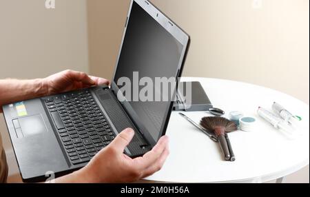 Hände des Reparaturmanns, der den ausgeschlossenen Laptop mit dunklem Bildschirm hält. Computerservice und -Reparatur. Demontage des Laptops in der Reparaturwerkstatt. Elektronische Entwicklung, Stockfoto