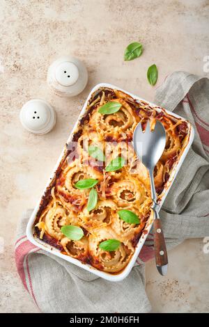 Lasagne. Hausgemachte Lasagne Pasta Rotolo mit Tomatensauce, Frischkäse und Basilikum auf weißer Pfanne auf hellem Schiefer, Stein oder Beton. ICH Stockfoto