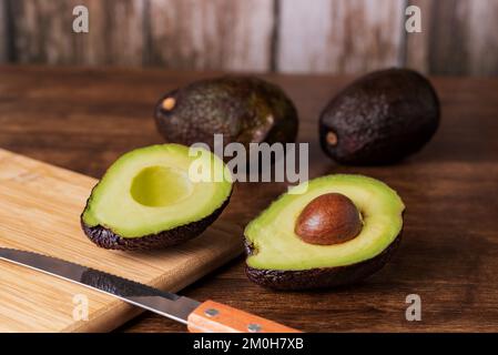 Mehrere Avocados auf einem rustikalen Holztisch, wobei eine der Avocados in zwei Hälften geteilt ist. Stockfoto