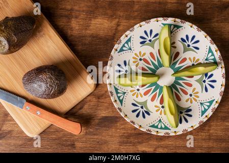 Avocado-Stücke auf einem rustikalen Teller auf einem Holztisch, begleitet von weiteren Avocados. Stockfoto
