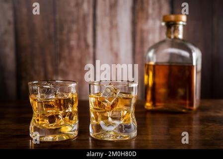 Zwei Gläser Whiskey mit Eiswürfeln, mit einer Flasche Whiskey im Hintergrund unscharf. Stockfoto