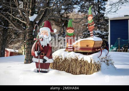 Weihnachtsdekoration mit einem weihnachtsmann und seinem Schlitten mit zwei Elfen auf einem Heuballen in einer verschneiten Winterlandschaft in Taylors Falls, Minnesota, USA. Stockfoto