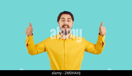 Porträt eines fröhlichen, gut aussehenden jungen Mannes, der mit beiden Händen Daumen nach oben zeigt Stockfoto