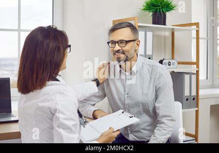 Arzthelferin im weißen Kittel spricht mit männlichem Patienten Stockfoto