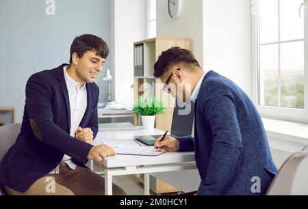 Mann unterzeichnet Leasing- oder Kaufvertrag, der ihm vom Bankmanager oder Immobilienmakler erteilt wurde. Stockfoto