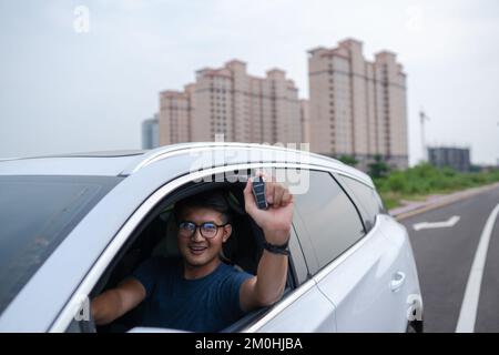 Der Asiate zeigt den Schlüssel eines innovativen Elektroautos Stockfoto