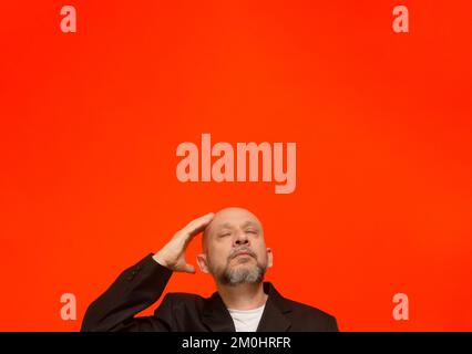 Geschäftsmann, trägt eine schwarze Anzugjacke, schlau und aufmerksam. Isoliert auf orangefarbenem Hintergrund. Stockfoto