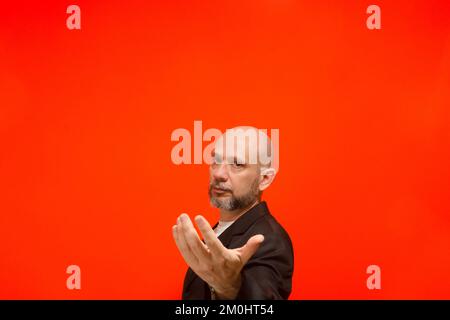 Porträt eines stilvollen Geschäftsmannes, der Handgesten macht. Ich schaue in die Kamera. Isoliert auf orangefarbenem Hintergrund. Stockfoto