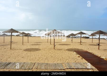 Regnerischer Tag am leeren Strand mit Wellen des atlantischen Ozeans und Sonnenschirmen Stockfoto