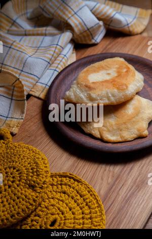 Tonplatte mit zwei einzelnen gebratenen Pasteten mit Fleisch auf Holztisch. Tatarische traditionelle Pasteten. Stockfoto