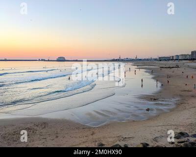 Matosinhos Beach bei Sonnenuntergang, entspannende Menschen, Stadtbild und Hafen Leixoes im Hintergrund, Porto, Portugal Stockfoto