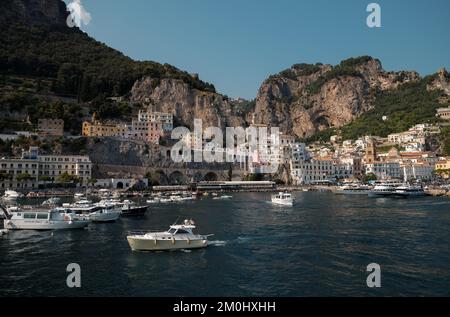 Panorama der Stadt Amalfi vom Hafen aus mit Blick auf die Stadt mit luxuriösen Motoryachten im Vordergrund und malerischen Klippen im Hintergrund. Stockfoto