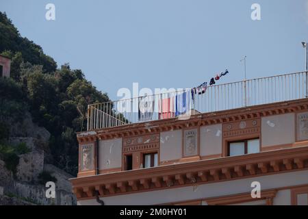Strandkleidung und Handtücher trocknen an einer Schlange auf einem traditionellen Dachbalkon in Amalfi, Italien Stockfoto