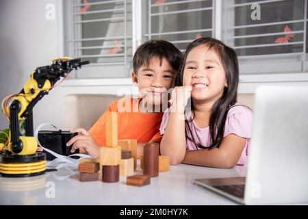 Kind kleines Mädchen programmiert Code für Roboter mit Laptop Computer und der Boy Test mit Fernbedienung, um Holzblock aufzunehmen Stockfoto