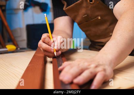 Ein Zimmermann, der nach dem Abmessen einer Holzplatte eine Bleistiftmarkierung macht Stockfoto