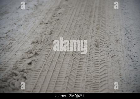 Schneereifenspuren. Asphalt mit Schnee bedeckt. Gefährliche Straßenbedingungen. Autoabdruck auf gefrorenem Boden. Reifenspur auf Eis. Stockfoto