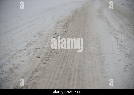 Radspuren auf der Winterstraße, die mit Schnee bedeckt ist. Stockfoto
