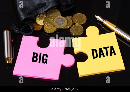 Geschäfts- und Finanzkonzept. Münzen sind auf der schwarzen Oberfläche verstreut, es gibt einen Stift und Rätsel, auf denen sie geschrieben sind - BIG DATA Stockfoto