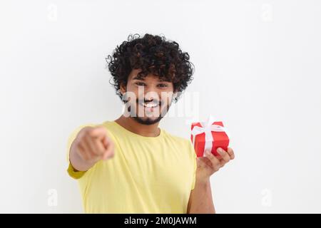 Ein asiatischer Mann mit lockigem Haar hält eine rote Geschenkbox, ein Lächeln, das auf die Kamera auf weißem Hintergrund schaut Stockfoto