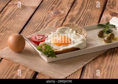 Frühstücksteller auf Holztisch. Rührei, Oliven, Tomaten und Gemüse auf Brot Stockfoto