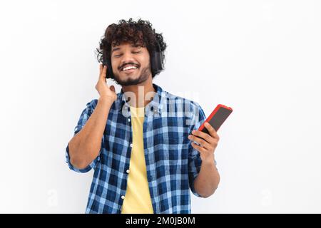 Glücklicher junger asiatischer Mann in lässiger Kleidung, der Musik mit Kopfhörern hört, hält ein Mobiltelefon Stockfoto