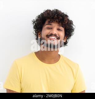 Mann mit lockigem Haar und fröhlichem Lächeln. Ein junger indischer Student, der fröhlich auf weißem Hintergrund steht Stockfoto