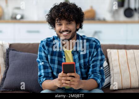 Ein asiatischer Mann, der ein Handy benutzt, sich online chattet, sitzt im Inder und hält ein Smartphone Stockfoto