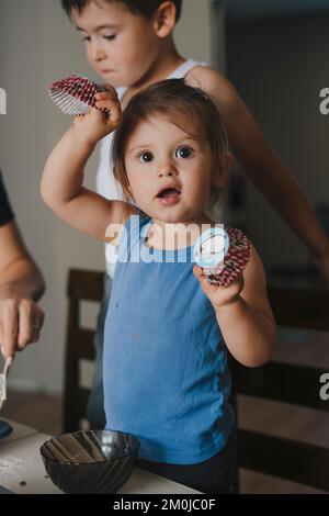 Mutter unterrichtet ein kleines, bezauberndes Kind, das Teig für hausgemachtes Gebäck zubereitet und zusammen in einer modernen Küche kocht. Die Familie kocht Muffins zusammen. Wie Niedlich Stockfoto