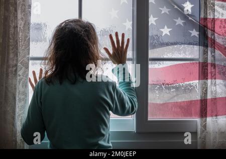 Frau am Fenster an Regentagen. Die US-Flagge außen. Bild: Weibliche Depression, häusliche Misshandlung, Menschenhandel, häusliche Gewalt, Psychische Gesundheit... Stockfoto