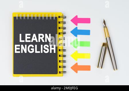Geschäfts- und Finanzkonzept. Auf weißem Hintergrund liegen ein Stift, Pfeile und ein Notizbuch mit der Aufschrift – LERNEN SIE ENGLISCH Stockfoto