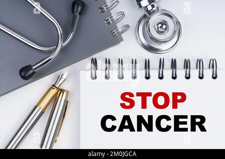 Medizin und Gesundheitskonzept. Auf dem Tisch befinden sich ein Stethoskop, ein Stift und ein Notizbuch mit der Aufschrift "STOP CANCER" Stockfoto