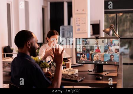 Ein afroamerikanischer Mann, der mit Kollegen im Online-Gruppenchat spricht, Kollegen begrüßt, Hi. winkt Büroangestellter diskutiert Startplan für Webcam-Meetings, Unternehmensvideos, Telearbeit Stockfoto