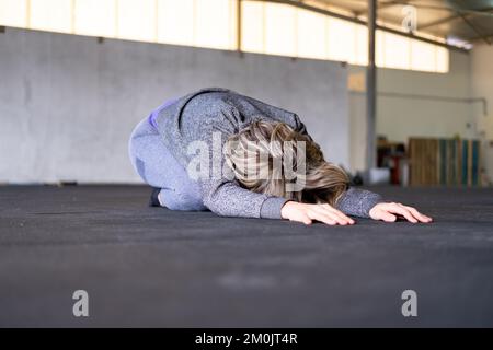 Eine blonde, mittelgroße Frau, die sich während ihres Vinyasa-Flow-Yoga-Trainings allein in der Kinderposition ausruht und Sportbekleidung im Fitnessstudio trägt. Stockfoto