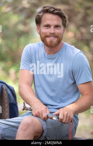 Ein junger Mann mit einem Messer schneidet einen Holzstock Stockfoto