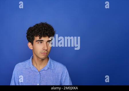 Porträt einer hübschen jungen Brünetten, ernsten Teenagerin auf blauem Hintergrund. Die Person wird in Kürze in einem Startup-Markt tätig sein. Stockfoto