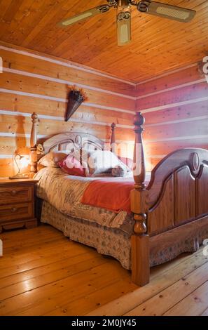 Antikes Himmelbett aus Holz und Nachttisch im Schlafzimmer im 1978 erbauten Nachbau des alten Blockhauses aus dem Jahr 1800er. Stockfoto