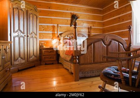 Antikes Himmelbett aus Holz und Nachttisch im Schlafzimmer im 1978 erbauten Nachbau des alten Blockhauses aus dem Jahr 1800er. Stockfoto