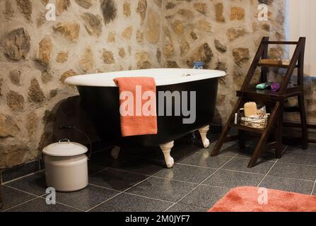Schwarz-weiße freistehende Badewanne und antike Möbel im Badezimmer im Nachbau des alten Canadiana Cottage-Stil Holz- und Feldsteinhauses. Stockfoto