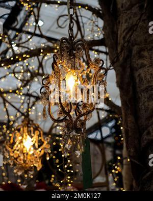 Wunderschöne Einrichtung mit Laternen und Girlanden draußen im Gartencafe. Laterne mit orangefarbenem Licht auf der Straße aus nächster Nähe. Dunkler Hintergrund mit Lampe in NI Stockfoto