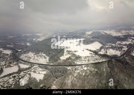 Luftige neblige Landschaft mit Bergstraße bedeckt mit frischem Schnee während heftigen Schneefällen im Winter Bergwald an kalten, ruhigen Tag. Stockfoto