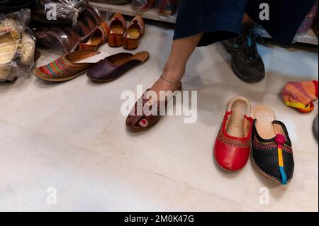 Schöne indische Frau, die ihren Fuß für das Anbringen von bunten Rajsathani Damenschuhen im Schuhgeschäft am berühmten Sardar Market und Ghanta Ghar Clock probiert Stockfoto